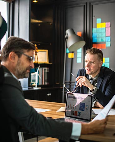 Two men in suits meeting at a desk with a computer in between them